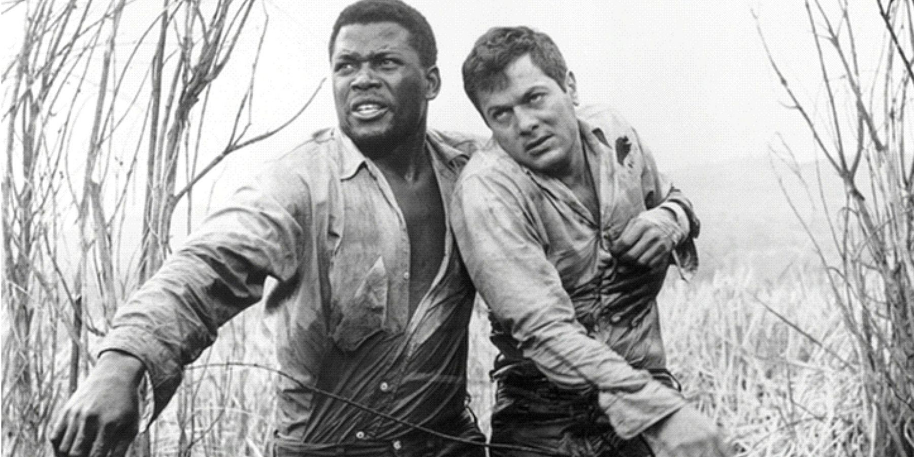Sidney Poitier and Tony Curtis chained next to each other and walking among bushes in The Defiant Ones