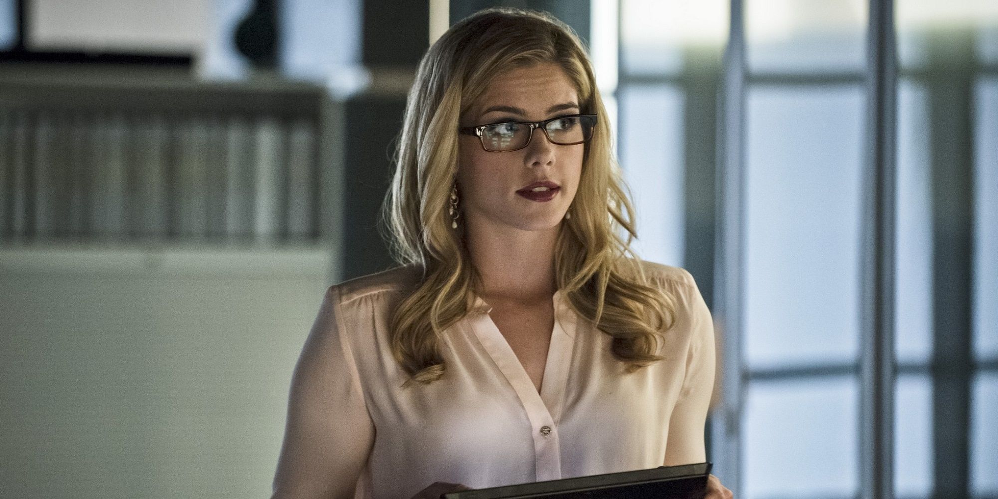 Felicity Smoak stands in the middle of an office with a tablet in Arrow