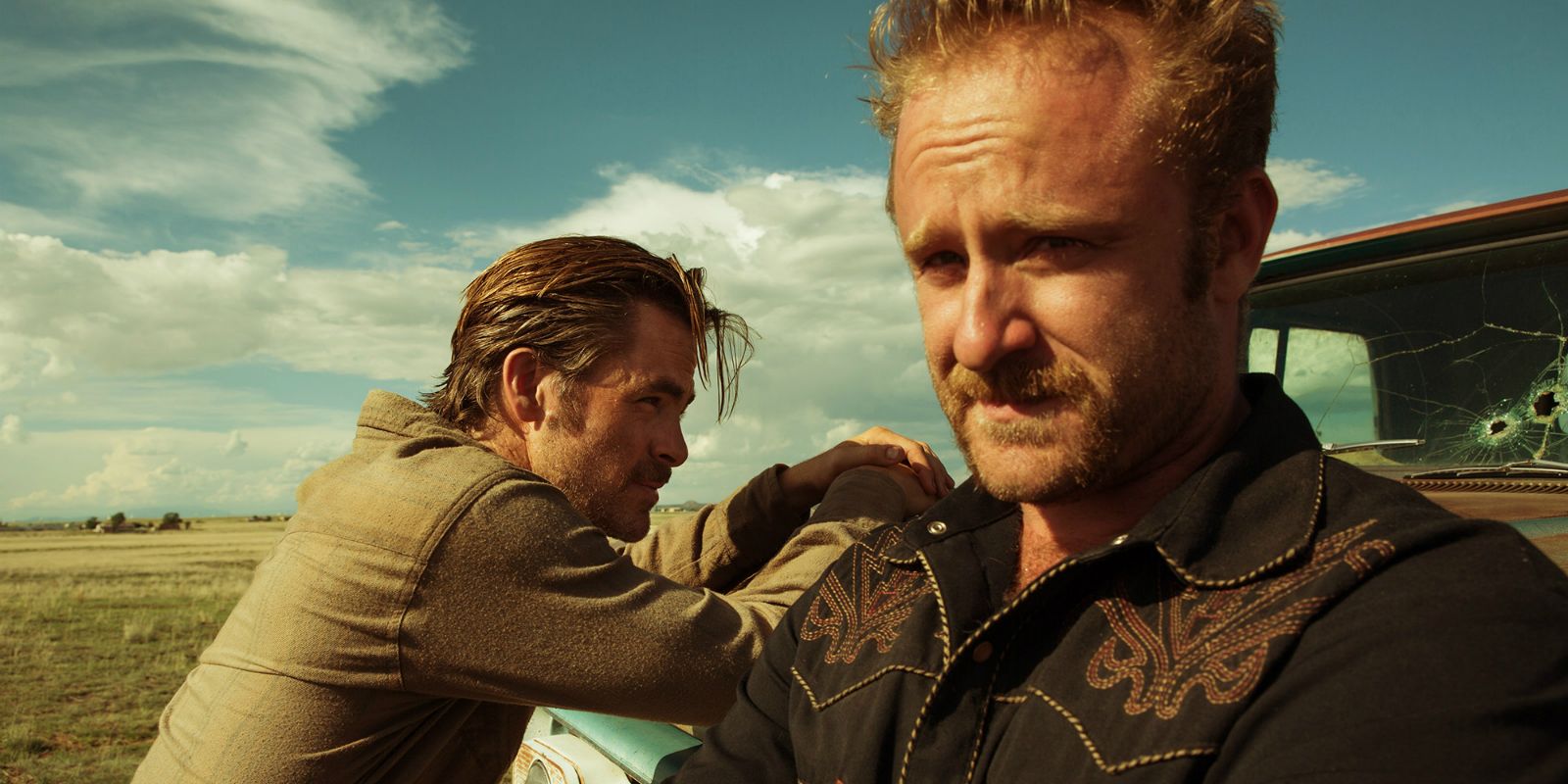 Ben Foster looking concerned with Chris Pine in the background leaning on a truck in Hell or High Water.