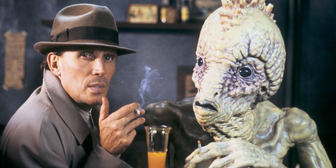 Peter Weller's William sits at a bar with a monster in Naked Lunch