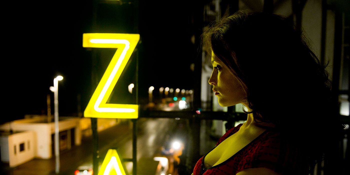 Gemma Artenton as Clara standing on a balcony in a corset overlooking an empty street in Byzantium