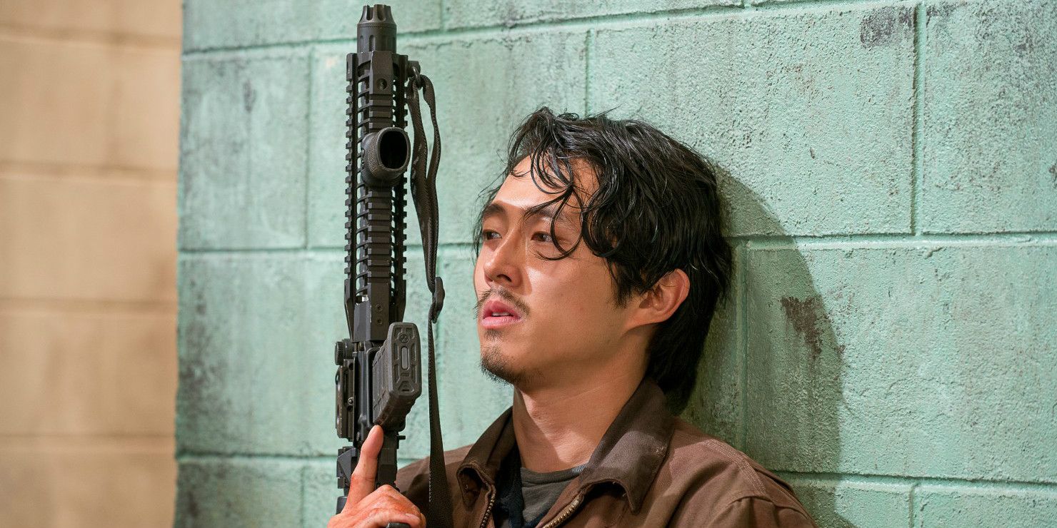 Glenn Rhee leans against a wall while holding a gun in The Walking Dead