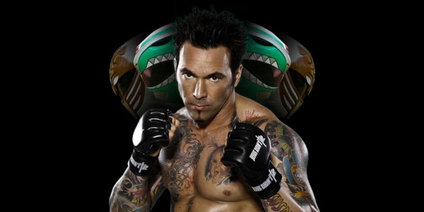Jason David Frank in gloves and shirtless in front of Power Rangers helmets