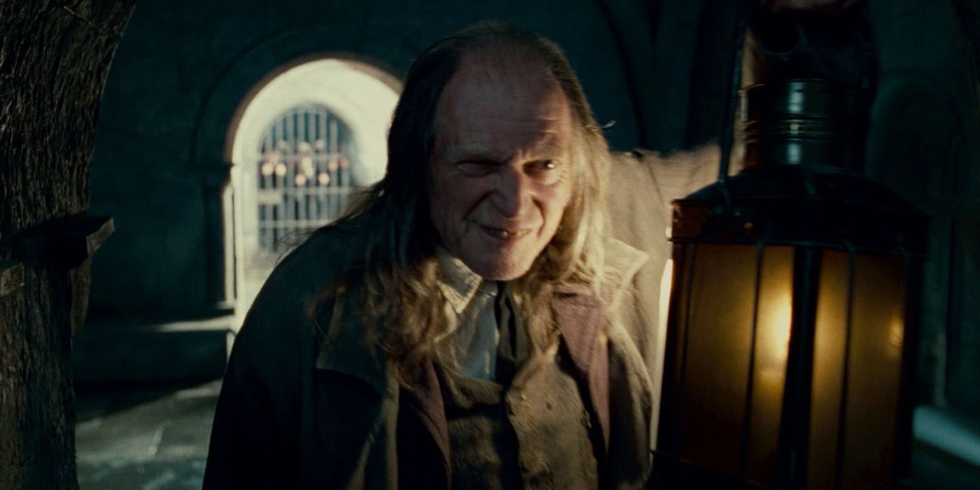 Argus Filch segurando uma lanterna em Hogwarts