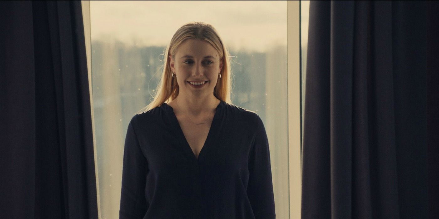 Greta Gerwig stands in front of a window and smiles in Mistress America