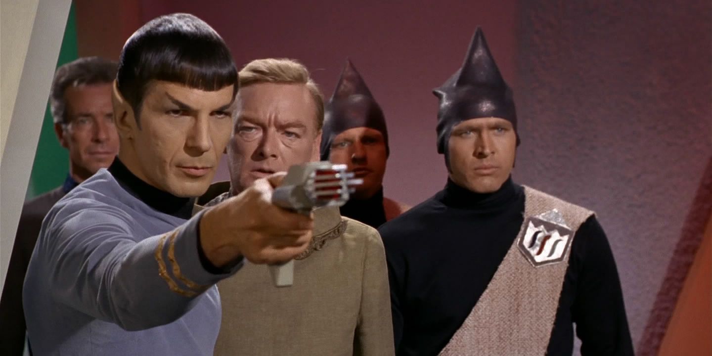 Spock points a gun as members of Eminiar VII look on