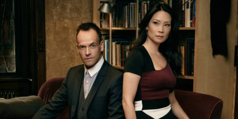 Sherlock Holmes (Jonny Lee Miller) and Joan Watson (Lucy Liu) posing in front of books in Elementary