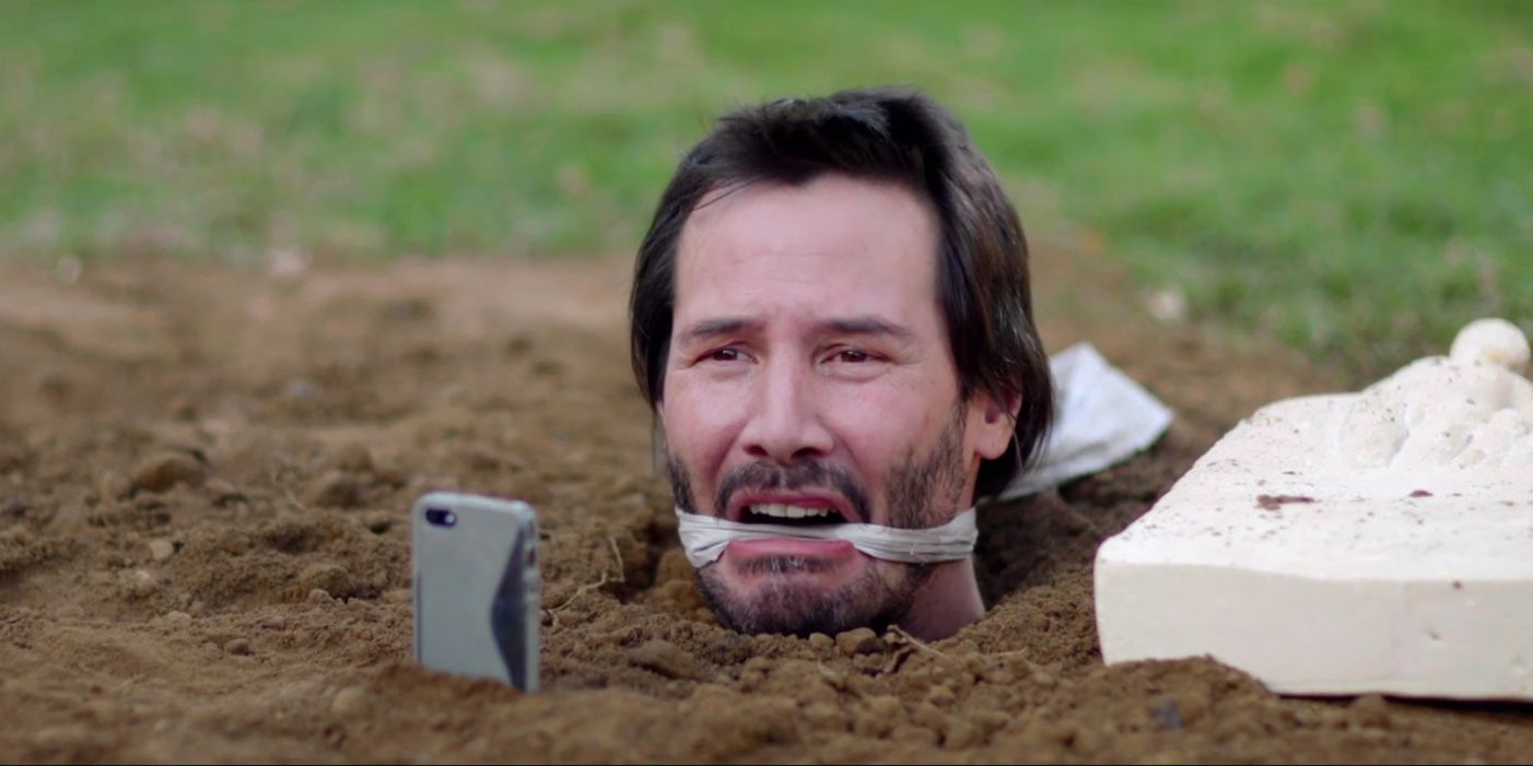 Keanu Reeves in Knock Knock buried up to his head.