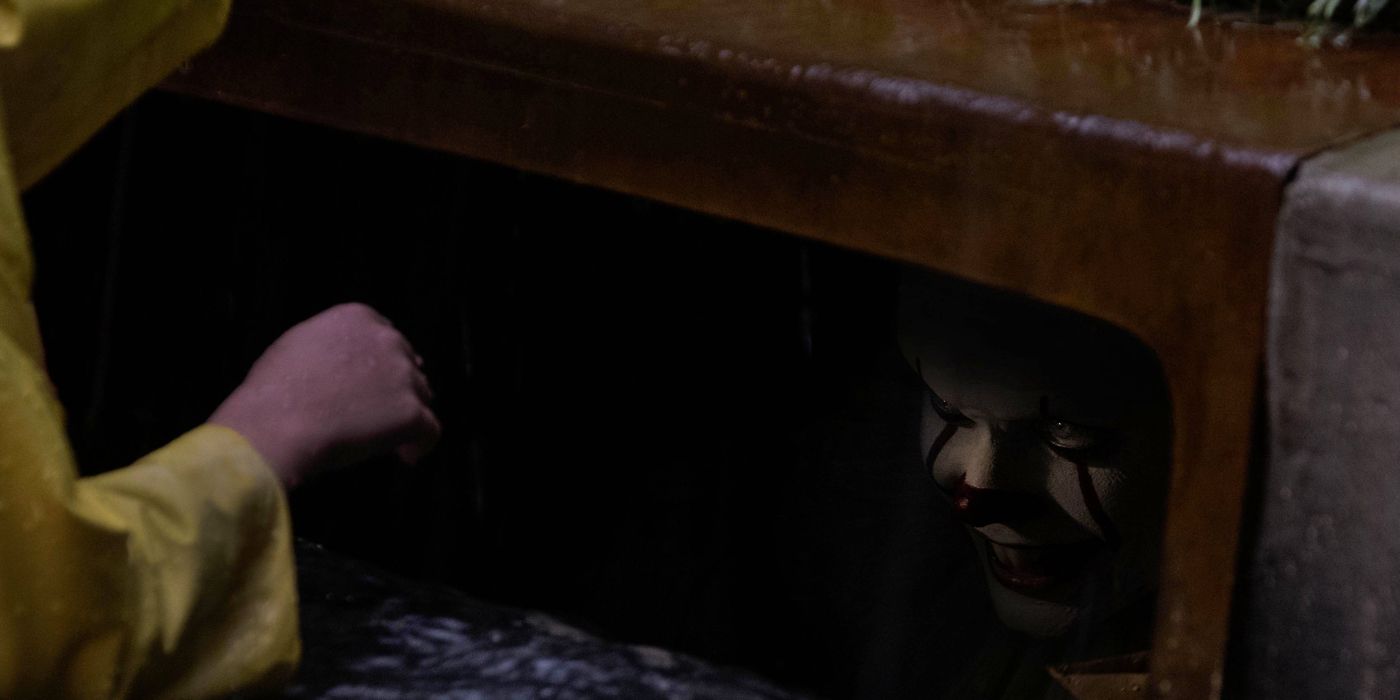 Pennywise smiles evilly as Georgie reaches into the sewer drain.