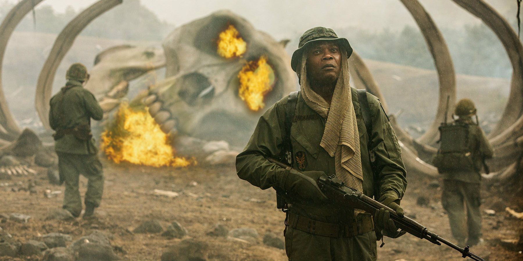 Samuel L. Jackson holds a rifle with a giant burning skull in the background