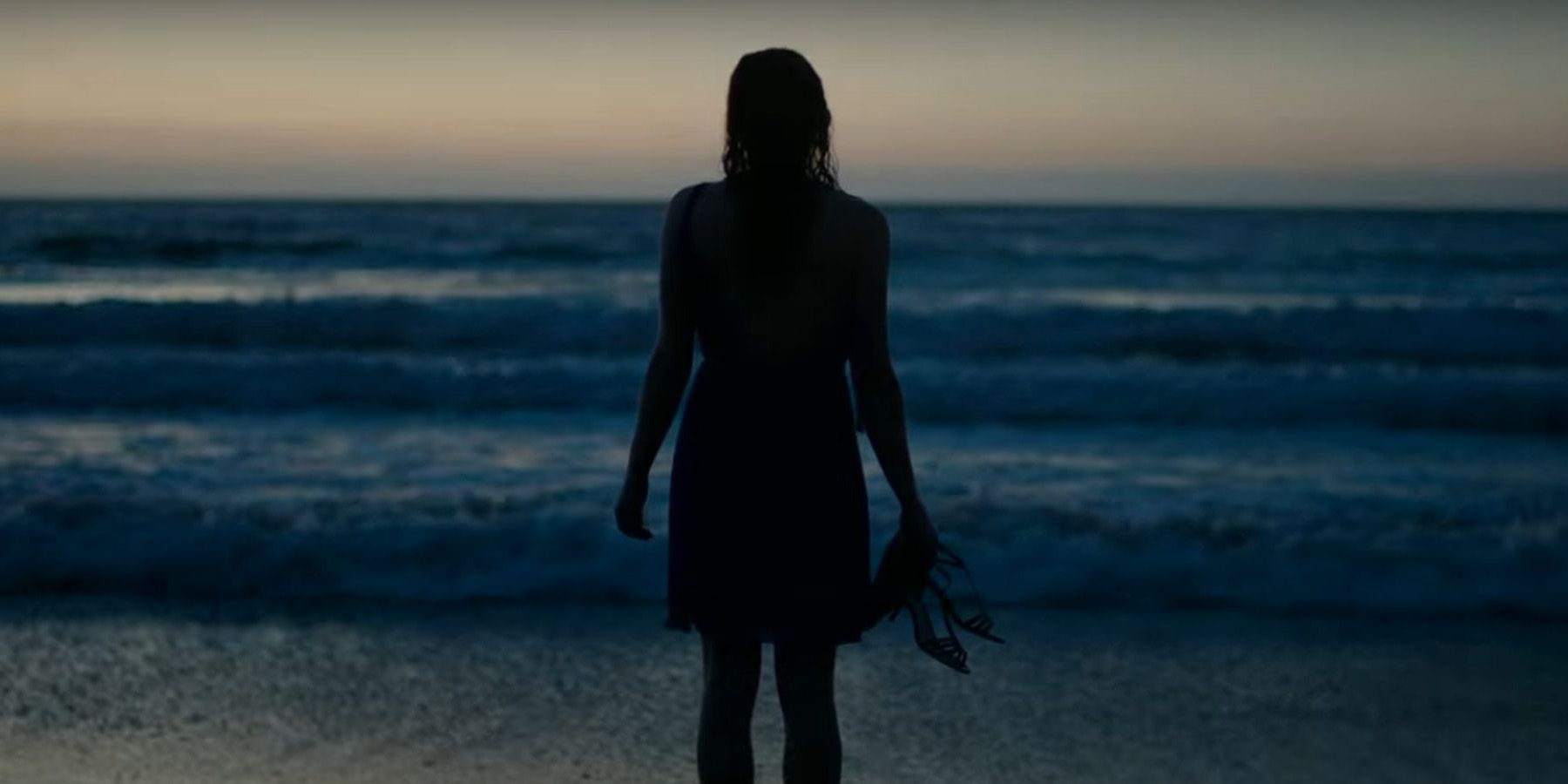 Shailene Woodley sebagai Jane dalam Big Little Lies berdiri di pantai dengan sepatu di tangannya.