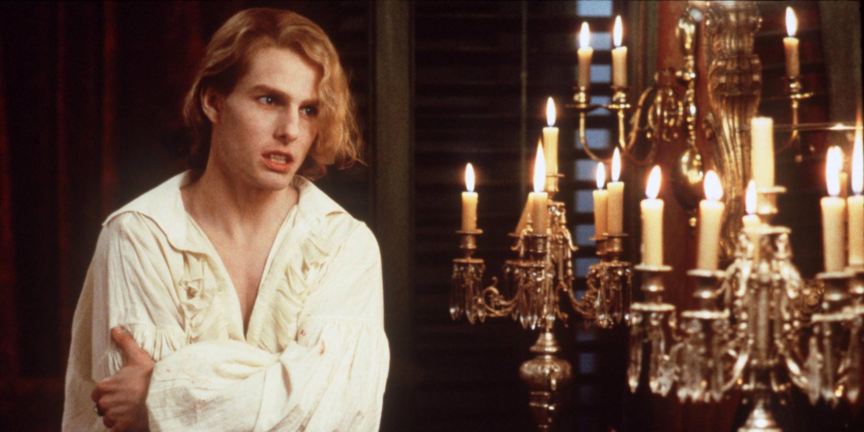 Lestat (Tom Cruise) grasping his arm next to a chandelier with lit candles in Interview with the Vampire