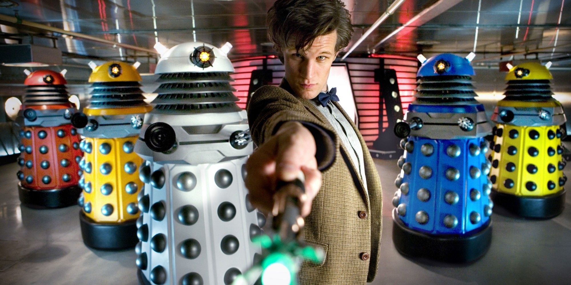 O Doutor posa na frente de uma fileira de Daleks multicoloridos de Doctor Who