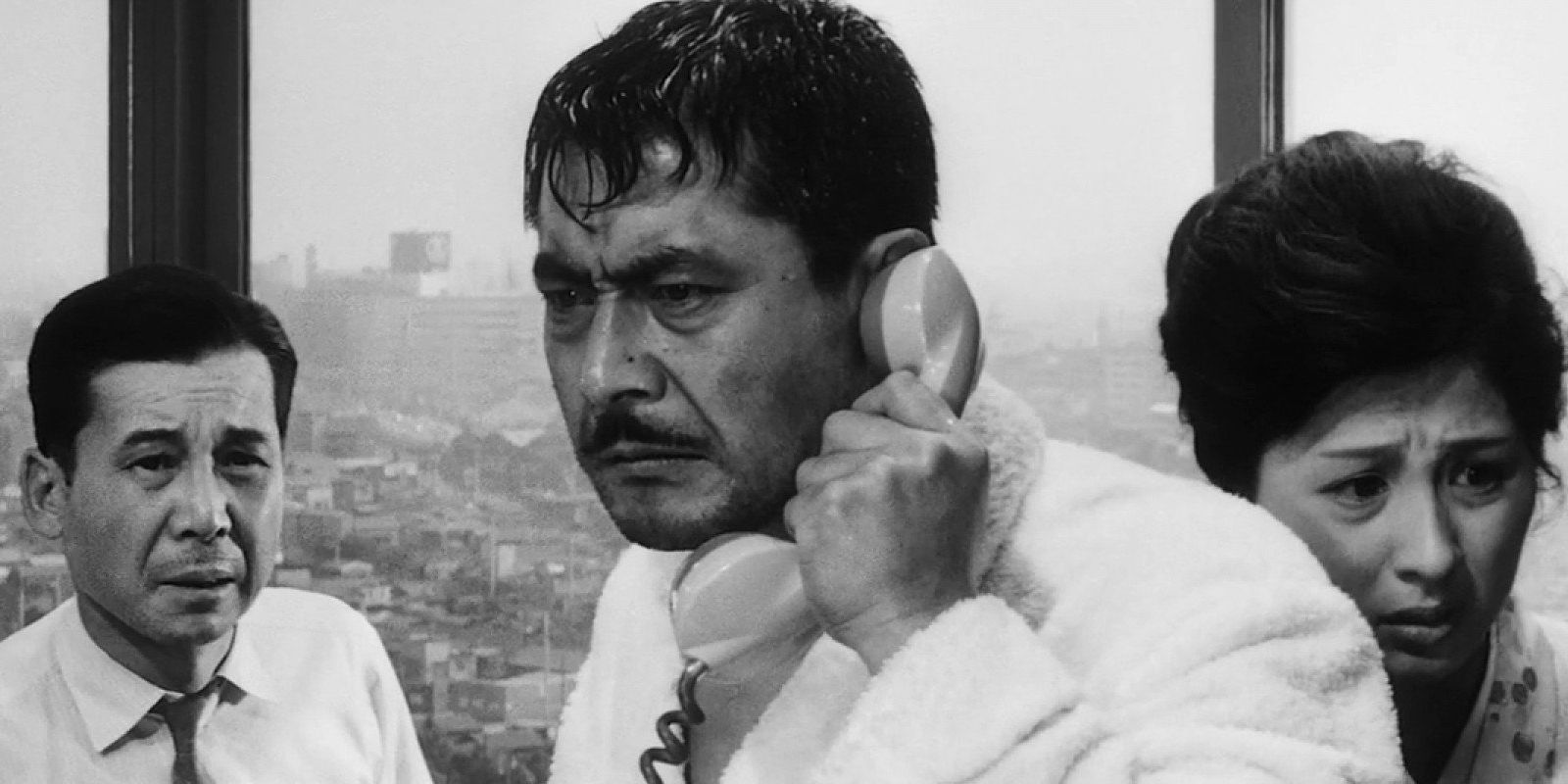 A man looking angry on the phone with two people behind him in High and Low