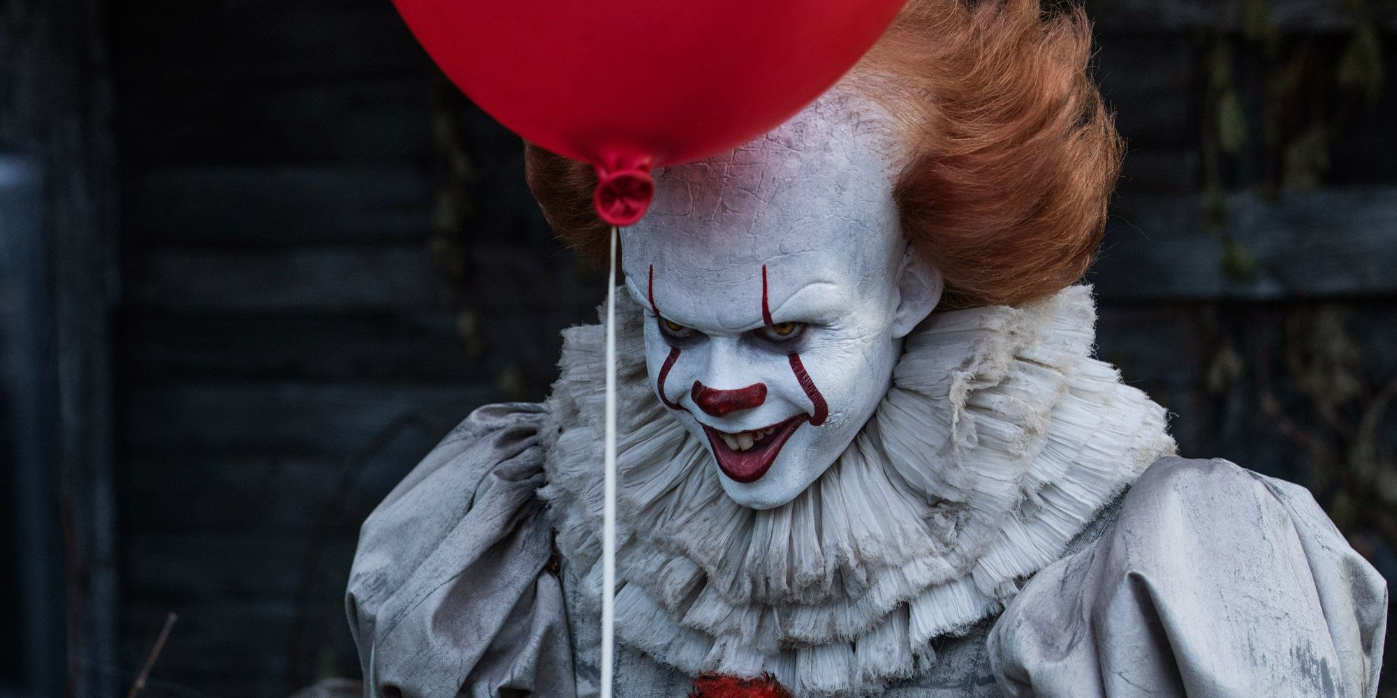 Pennywise smiling and holding a red balloon in IT