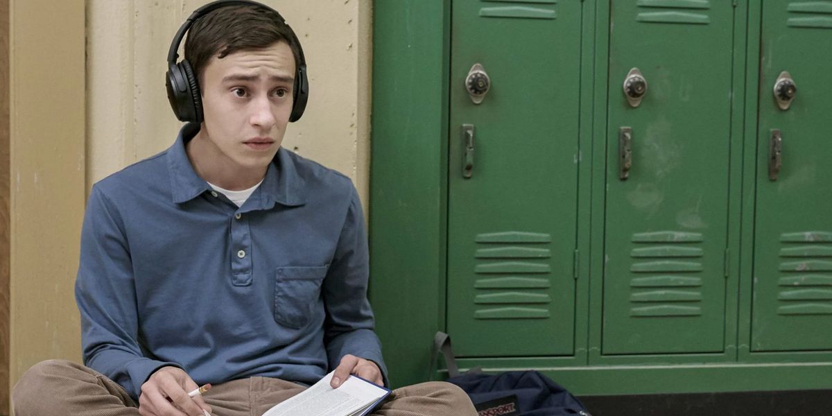 Sam Gardner sits on the hallway floor in front of lockers and wearing headphones in Atypical