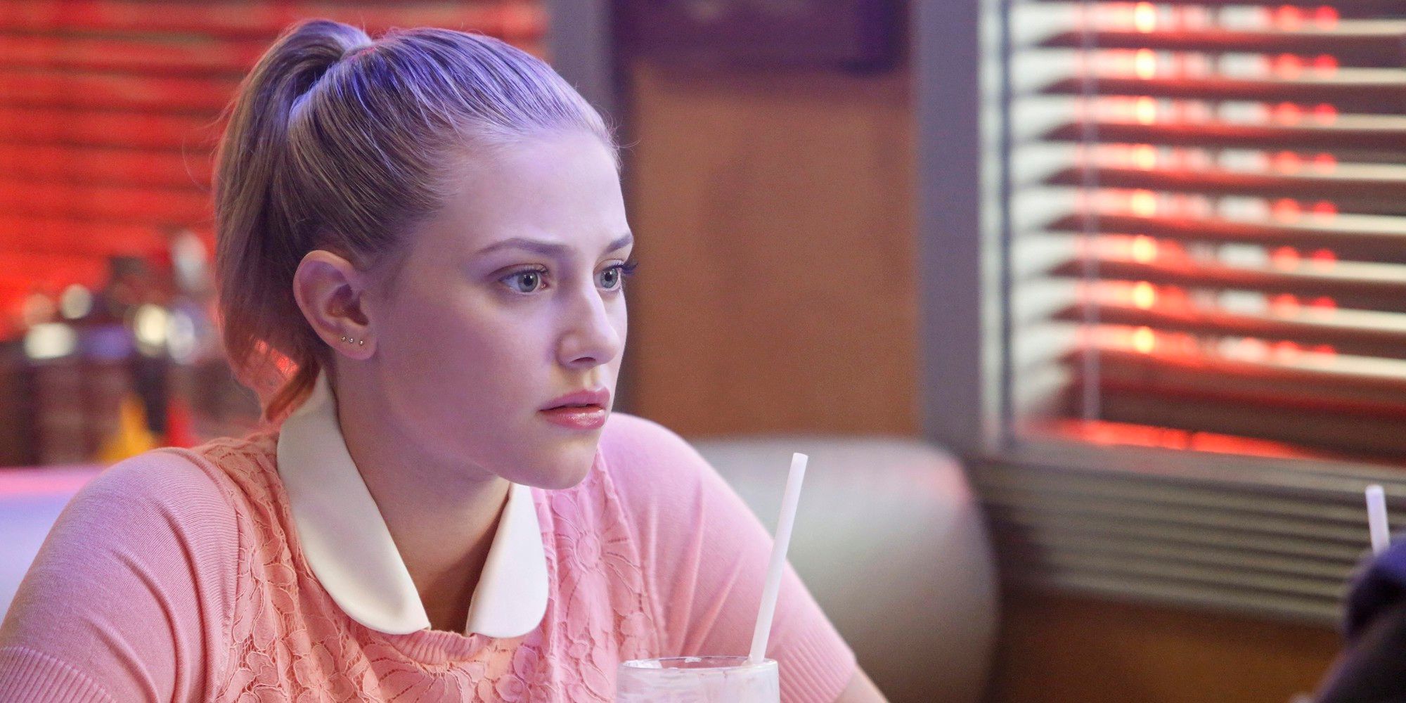 Betty from Riverdale sitting in the dinner, staring into space.
