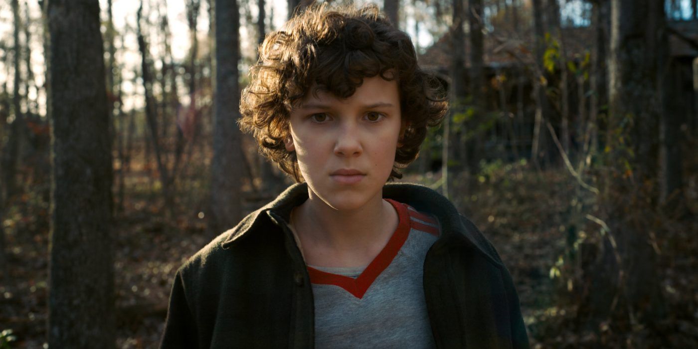Eleven standing in the woods looking serious in Stranger Things