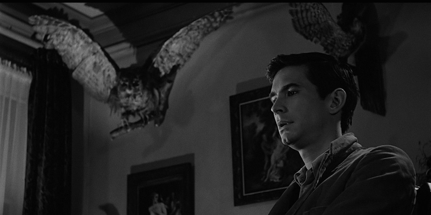 Anthony Perkins como Norman Bates em Psycho em um quarto escuro com corujas taxidermizadas.