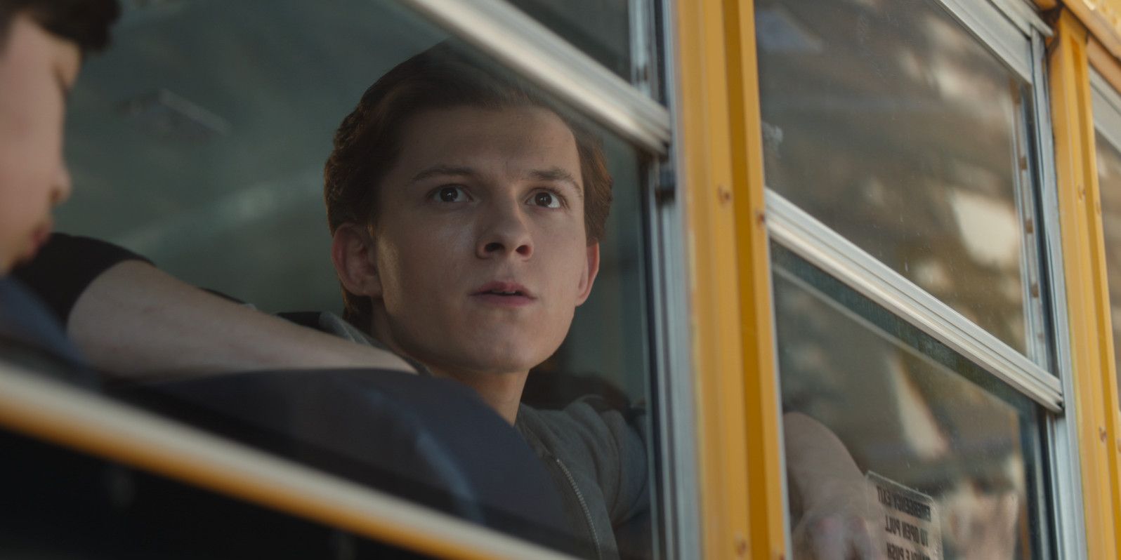 Peter Parker on a school bus noticing an alien spacecraft in the distance off-screen.