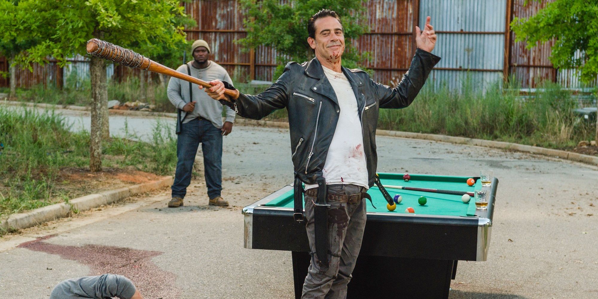 Negan standing in Alexandria, arms outstretched holding Lucille with a pool table behind him.