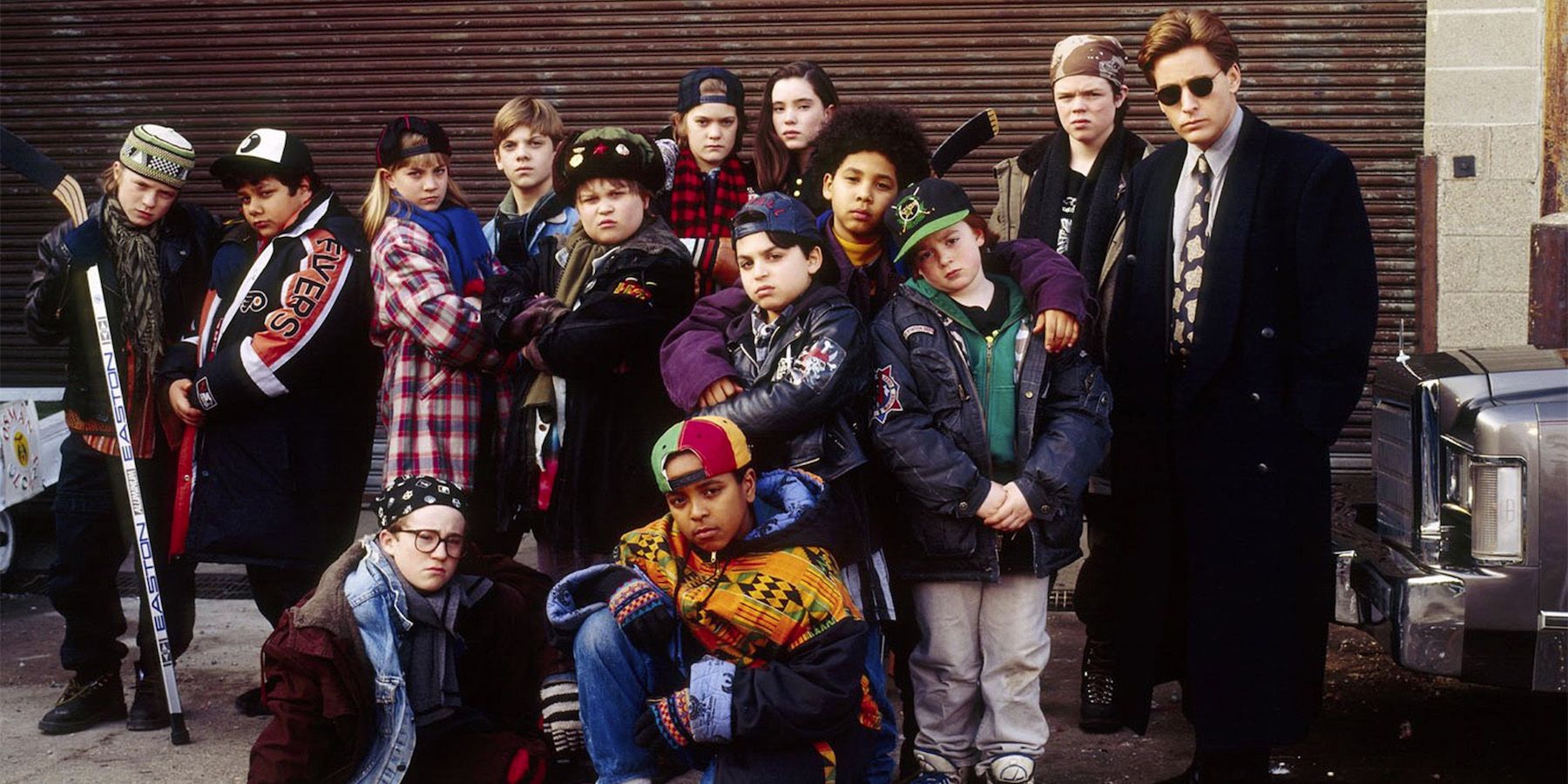 Bombay poses with his original Mighty Ducks team in an alley against a brick wall