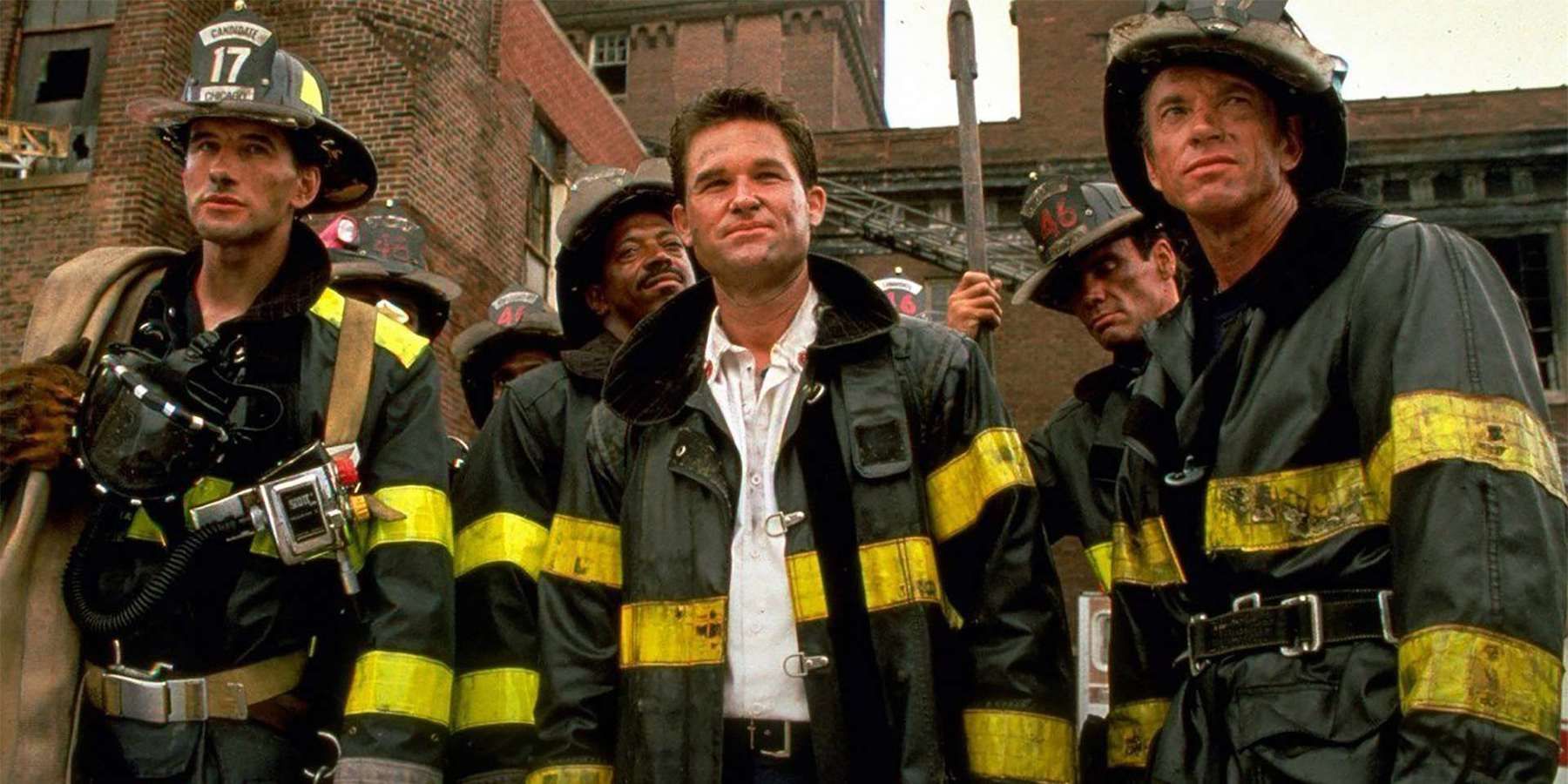 Kurt Russell como Stephen McCaffrey está rodeado por otros bomberos en Backdraft mirando hacia adelante y hacia arriba.