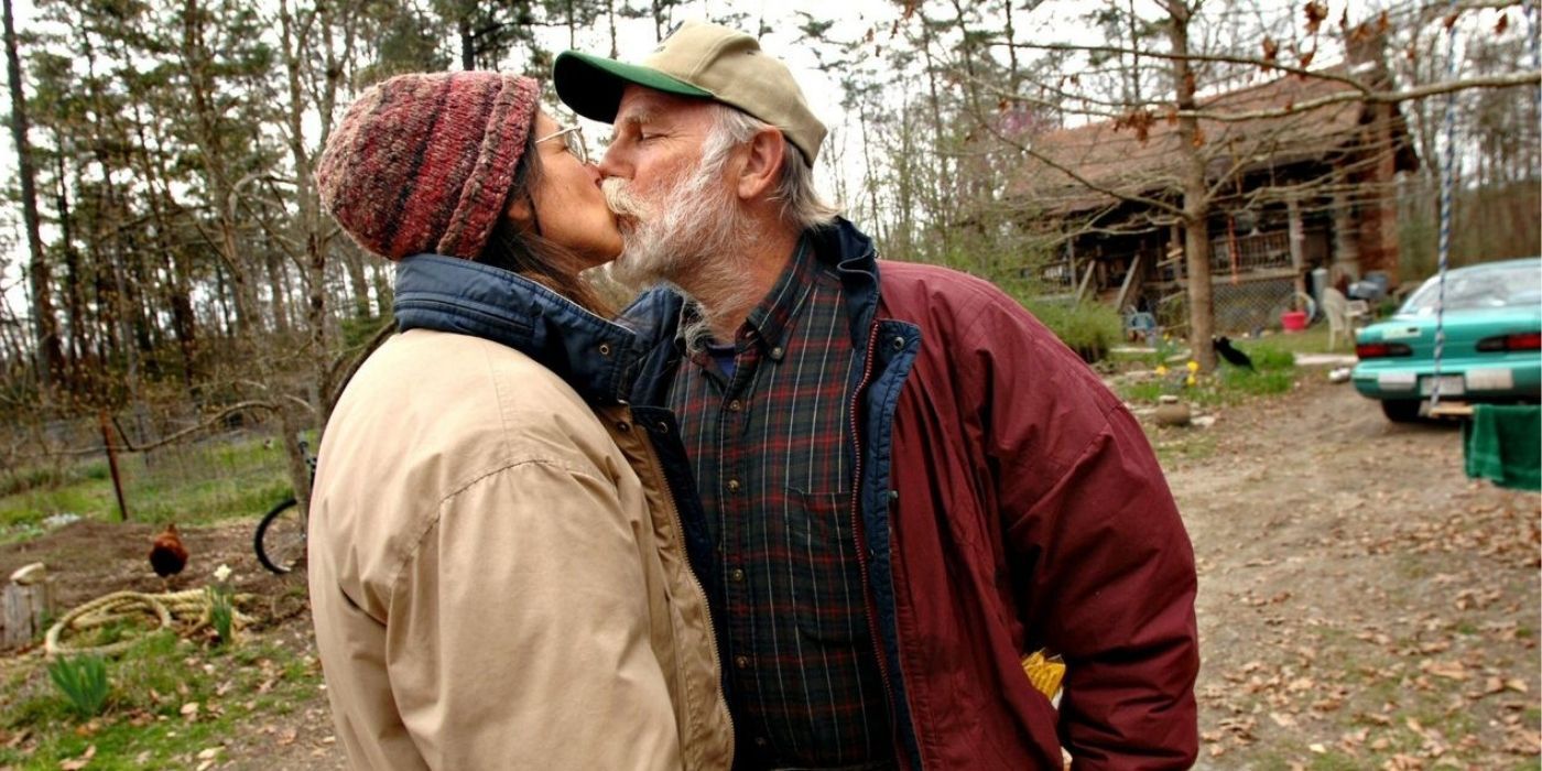 A Wife Swap kissing in the woods outside of their home