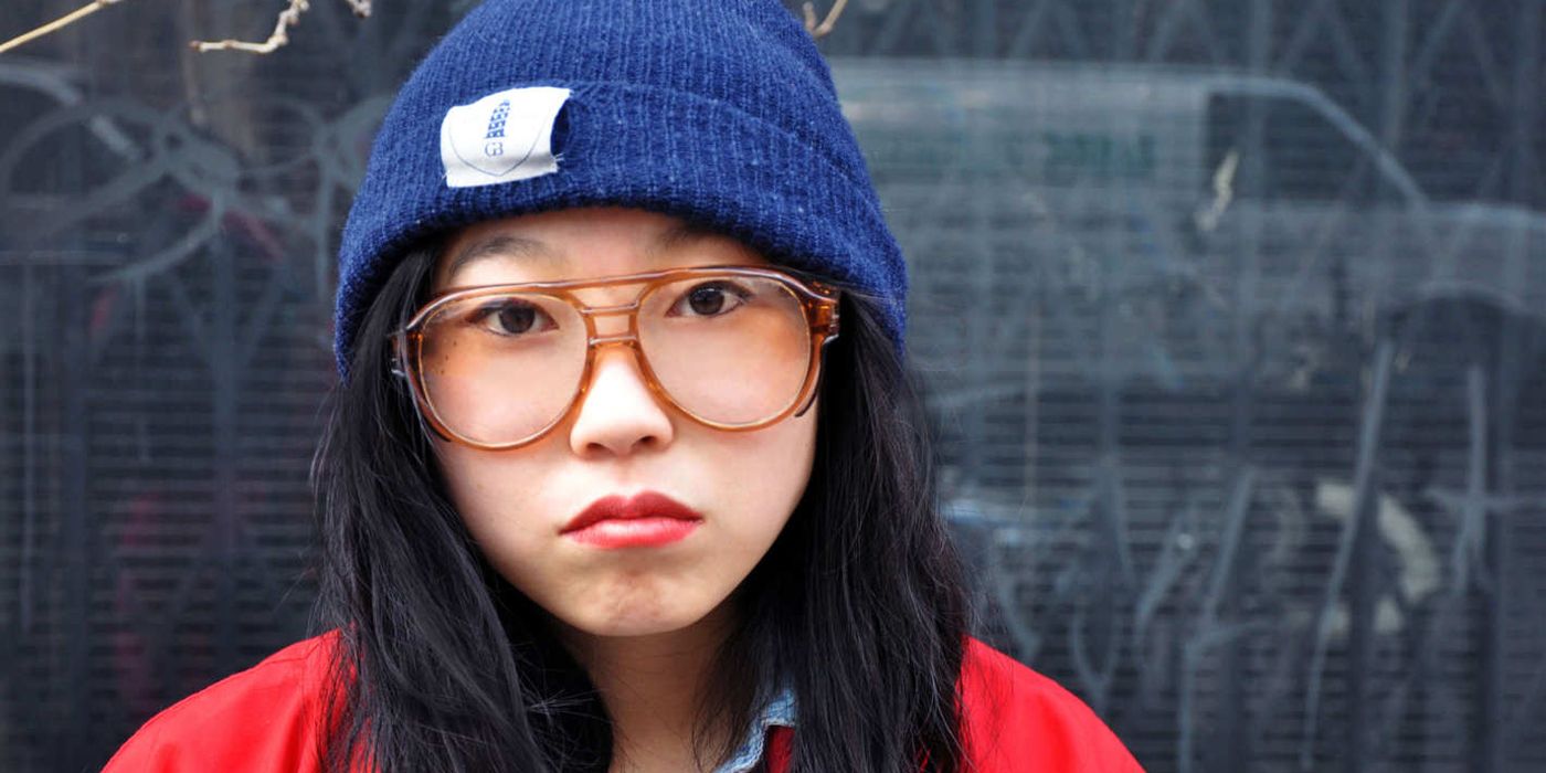 Awkwafina wearing a toque/beanie and glasses and looking at the camera.