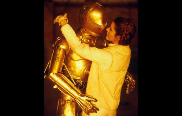 Carrie Fisher as Princess Leia kisses C3P0