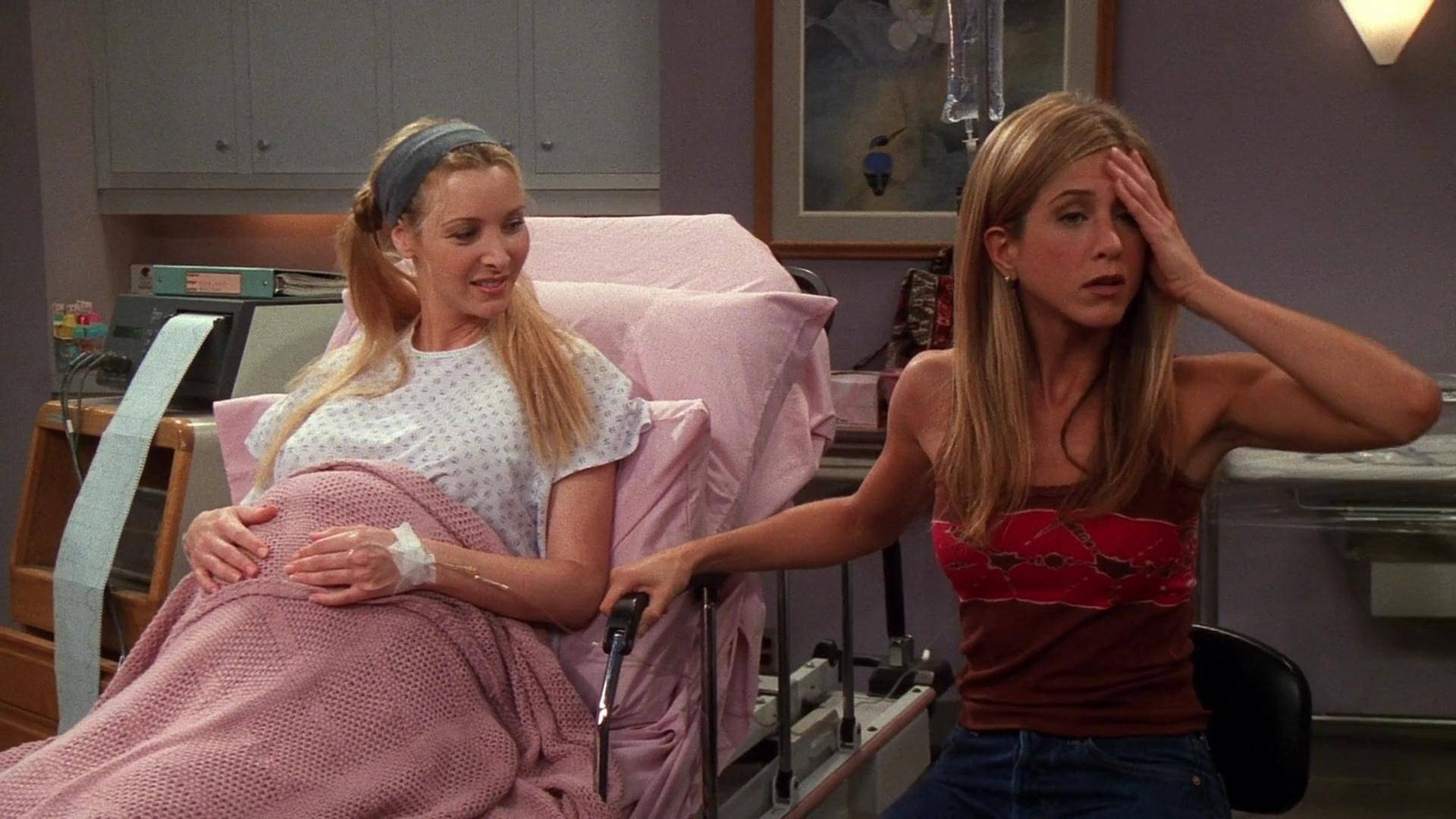 Phoebe sentada em uma cama de hospital com Rachel em Friends