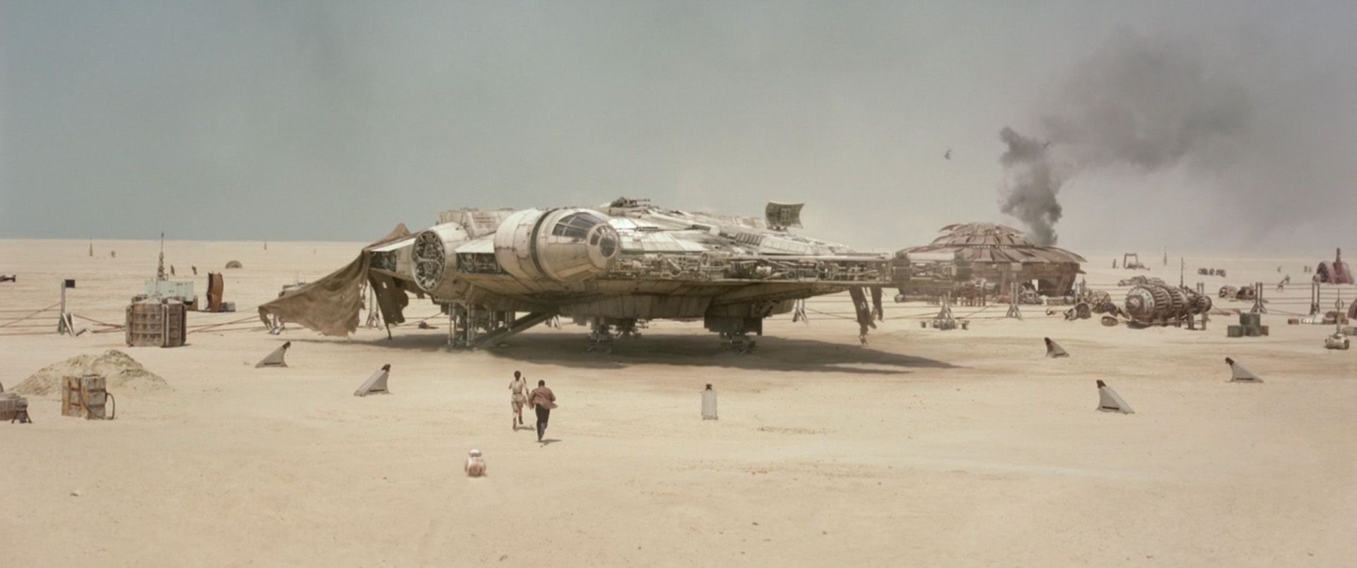 Rey, BB-8, and Finn run to the Millennium Falcon on Jakku in Star Wars The Force Awakens