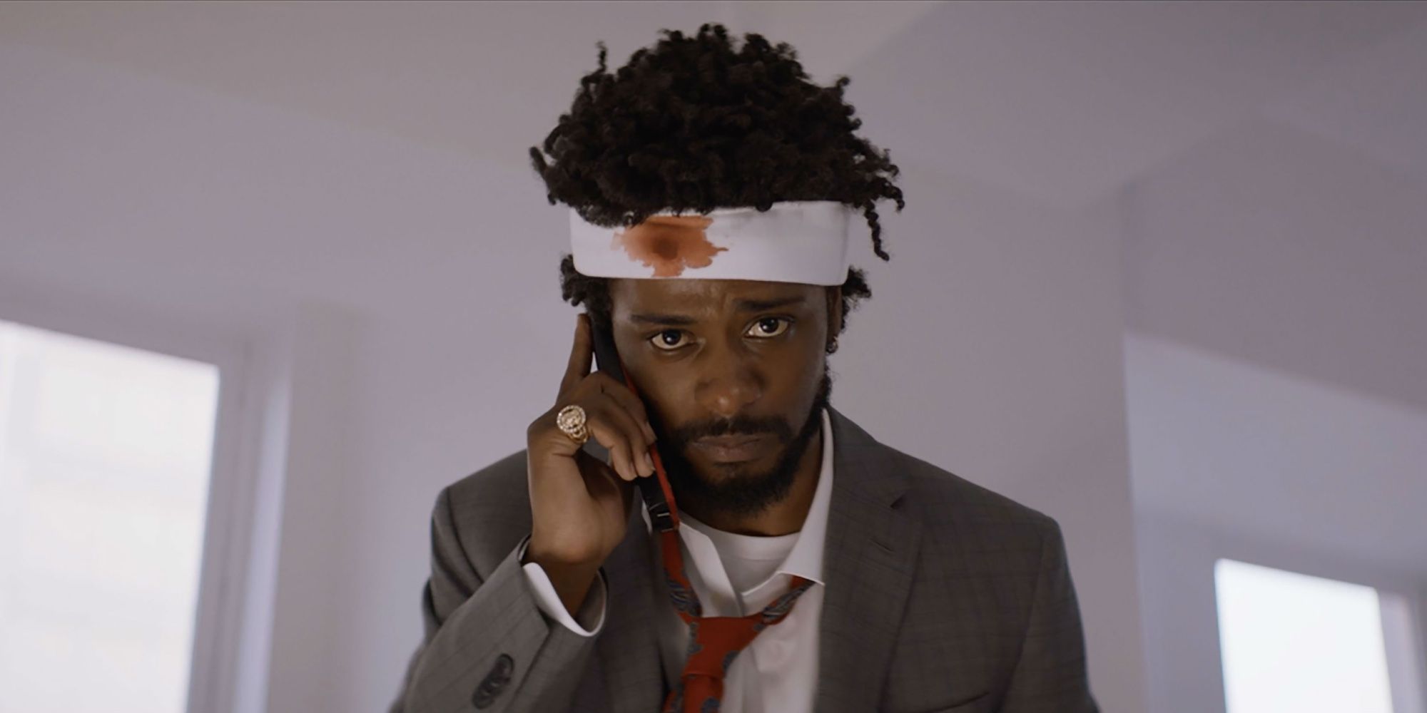 An injured man with a bandage on his head making a call in the movie Sorry To Bother You 