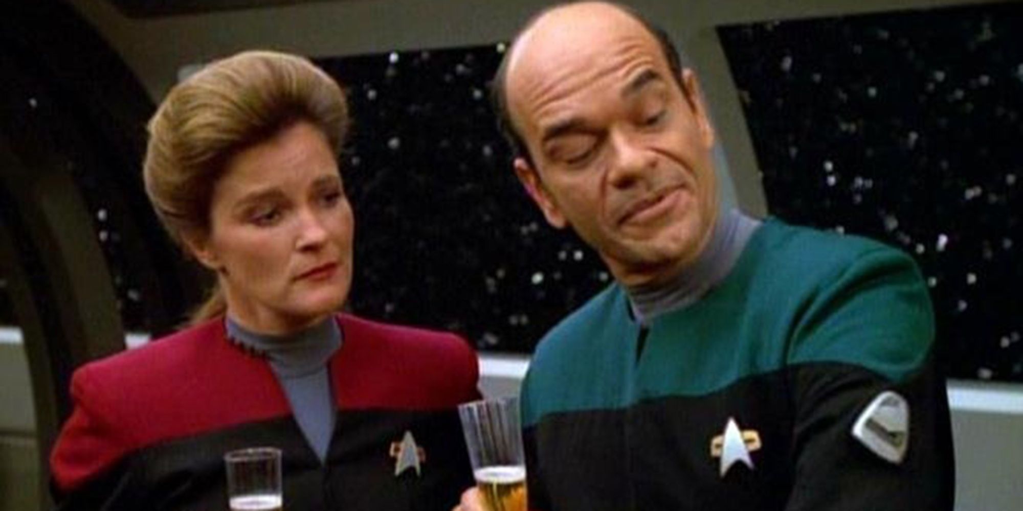 Capitão Janeway e o Doutor estão no refeitório com copos de champanhe admirando o emissor móvel do Doutor em Star Trek: Voyager epispode "Fim do futuro"