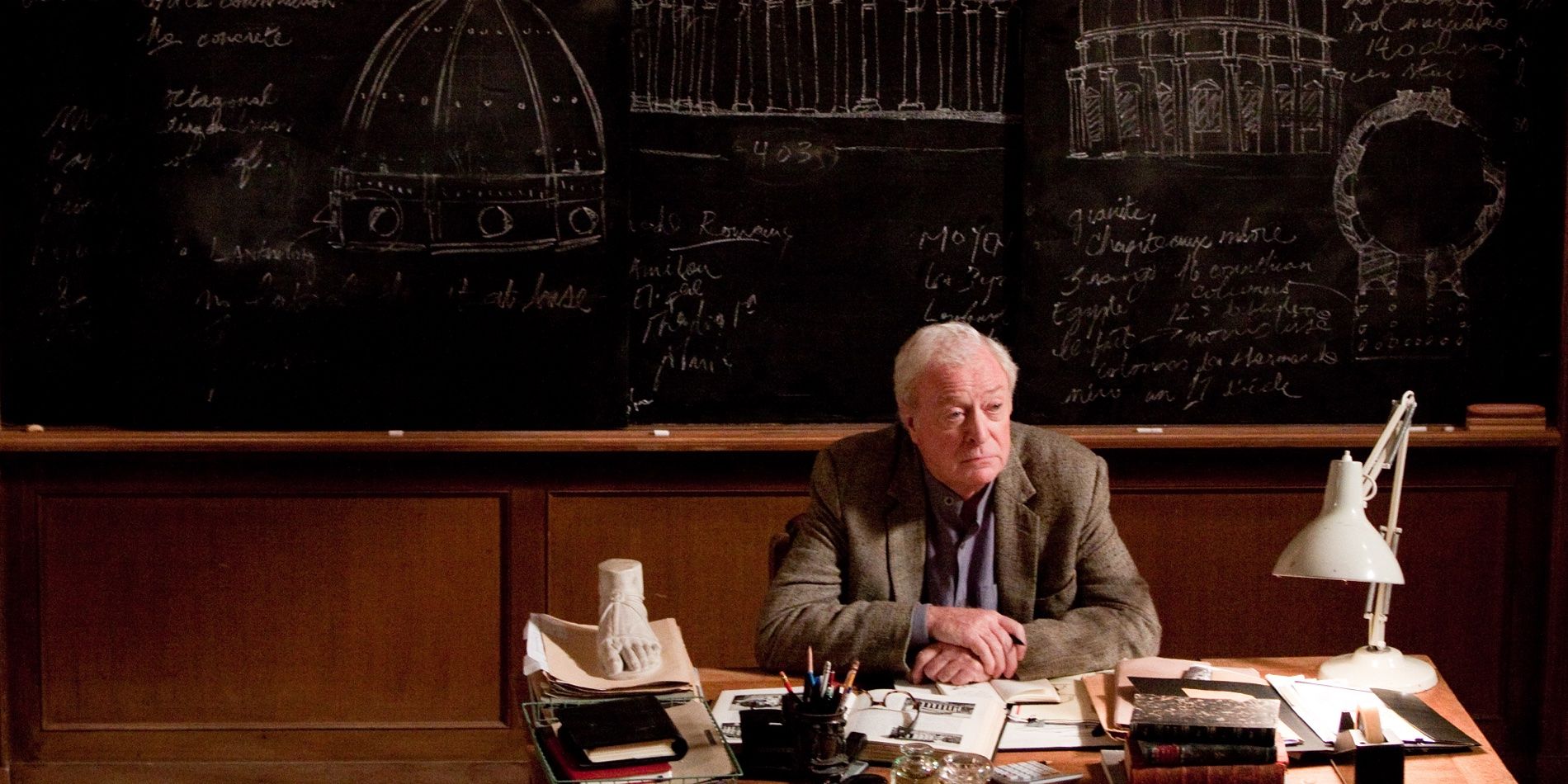 Michael Caine sitting behind a desk in Inception