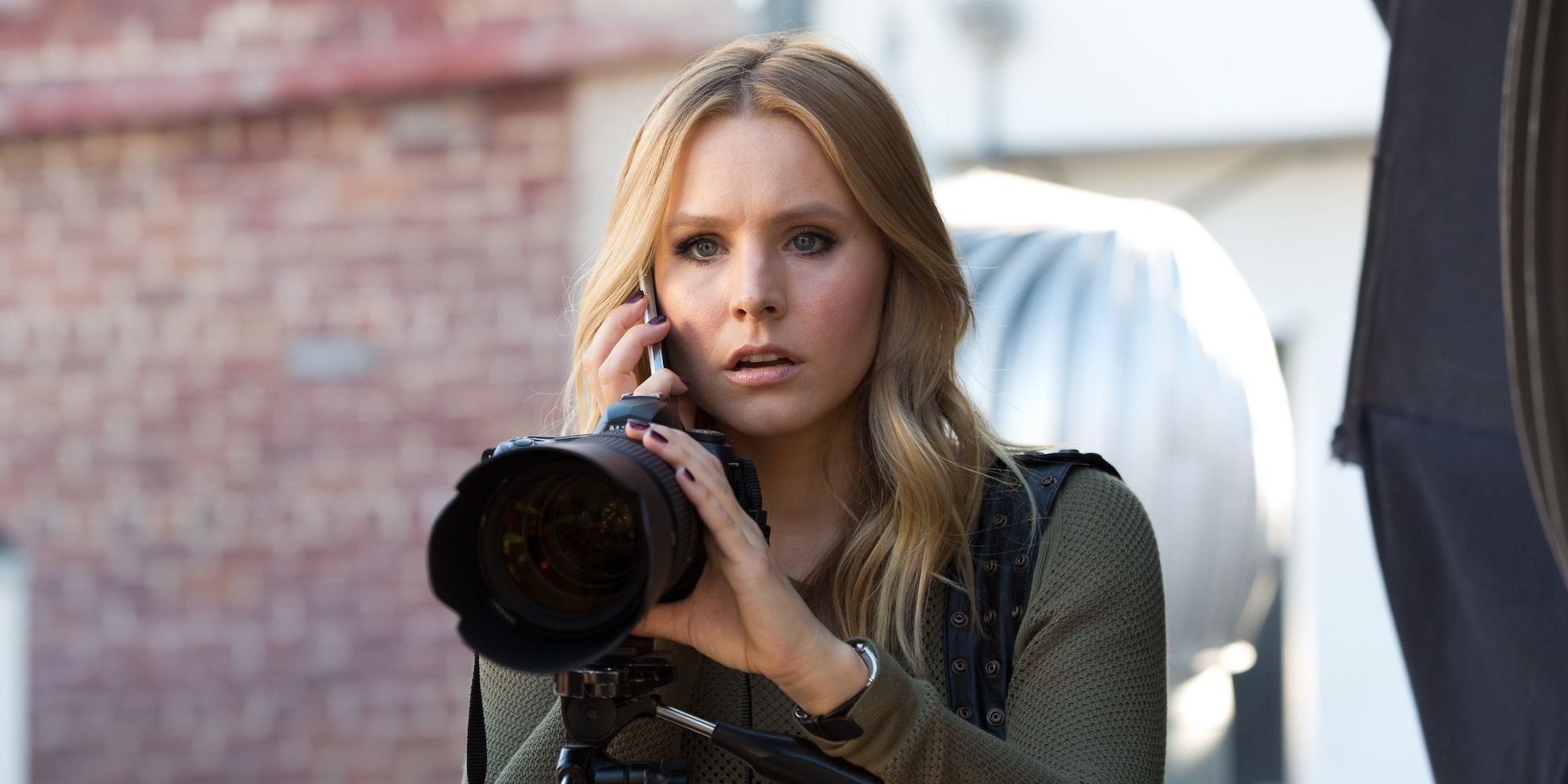 Kristen Bell como Veronica Mars segurando uma câmera e falando ao telefone no filme de 2014