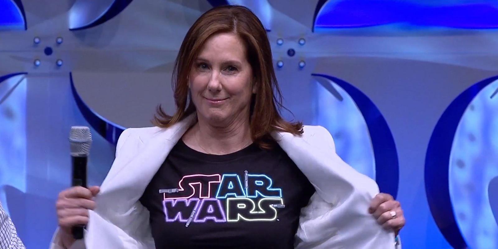 Kathleen Kennedy reveals a colorful Star Wars logo shirt underneath her white jacket at a Star Wars event.