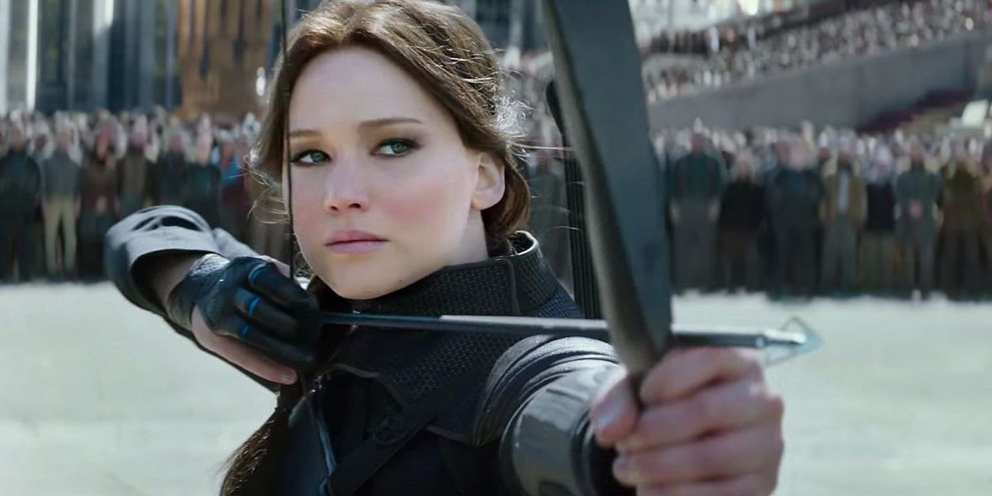 Katniss aiming her bow and arrow while a crowd watches in The Hunger Games.