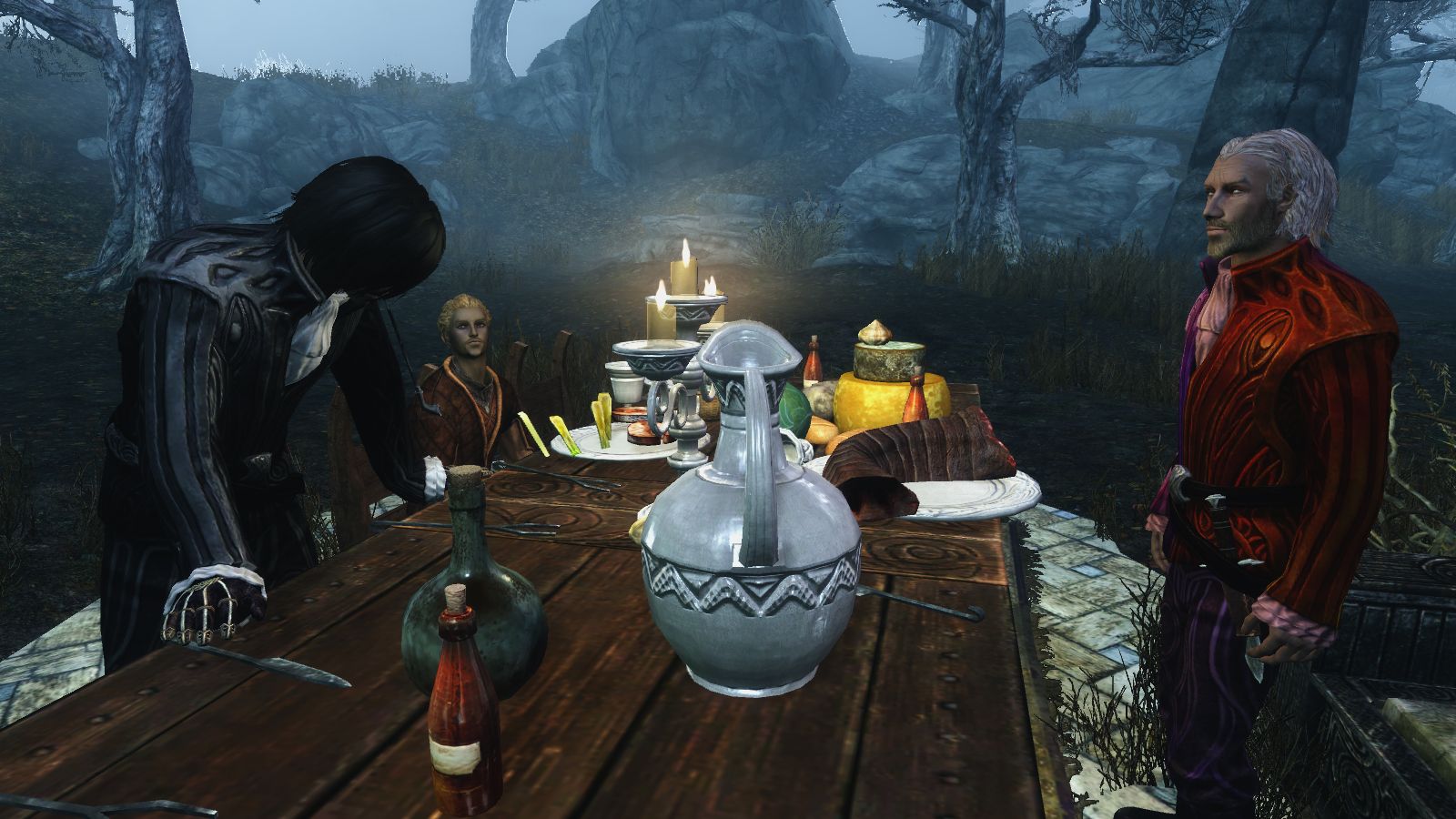 Three Skyrim characters are around a table, two standing and one sitting, the table is covered in food, candles, bottles and pitchers.