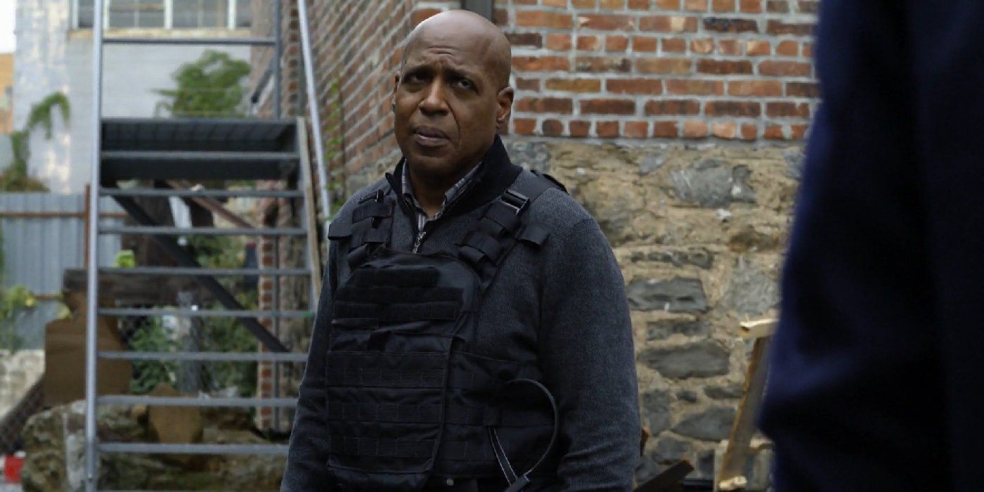 Vance wearing a jacket and a bullet proof vest standing in front of stairs in Manifest.