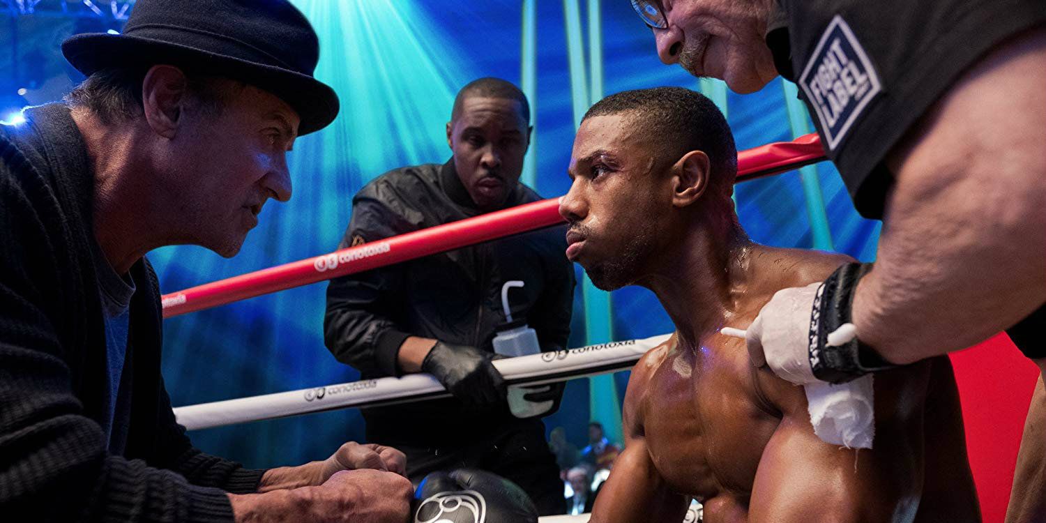 Adonis Creed sentado em um banquinho olhando para Rocky Balboa durante uma luta em Creed 2.