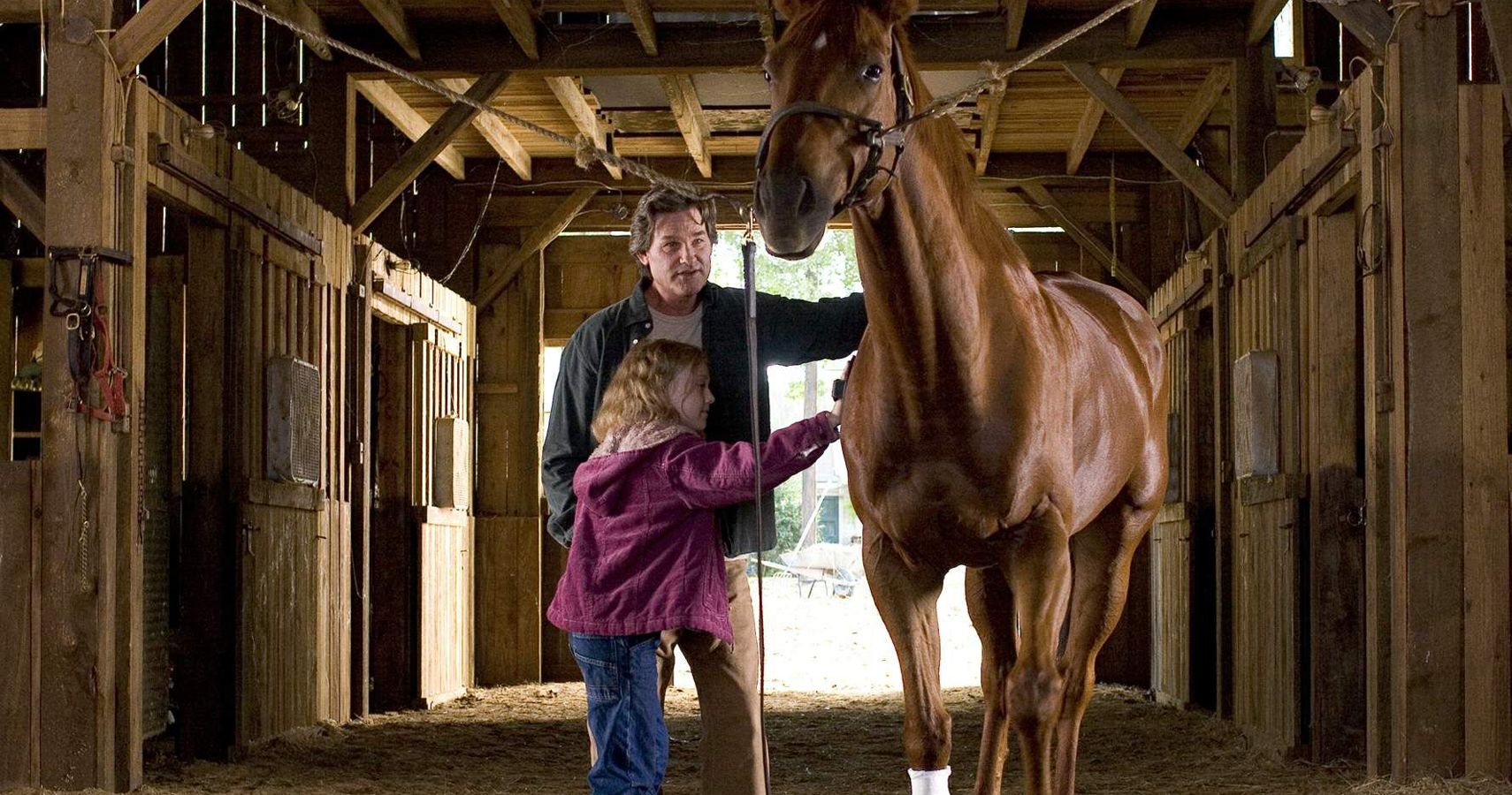 A man and a young girl pet a pretty horse in a barn in the movie Dreamer