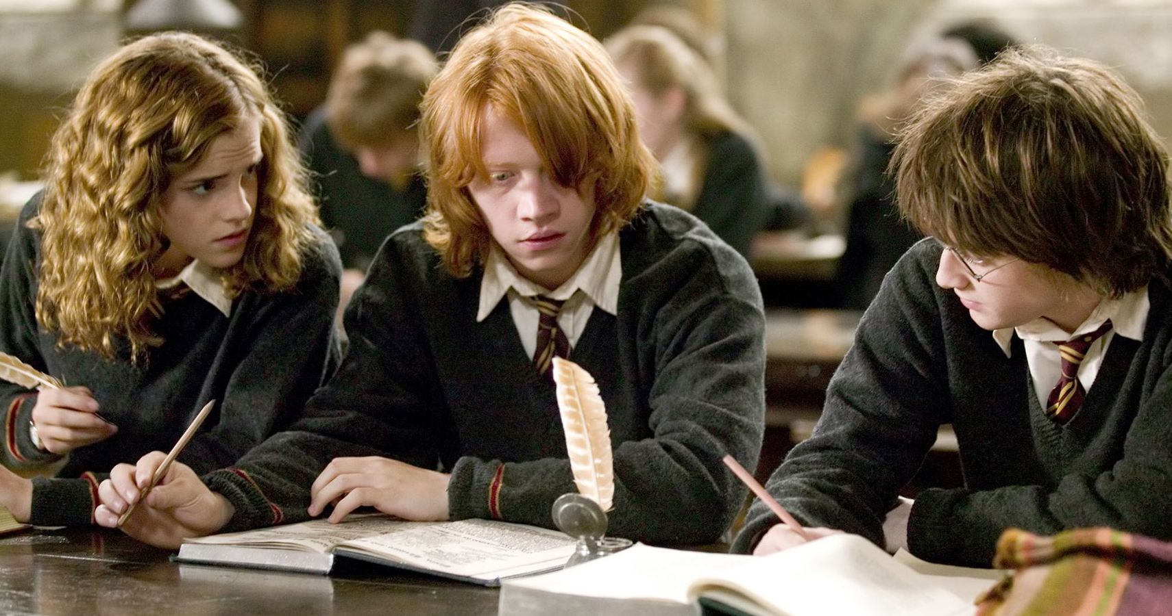 Hermione Granger, Ron Weasley, and Harry Potter studying in the Great Hall of Hogwarts