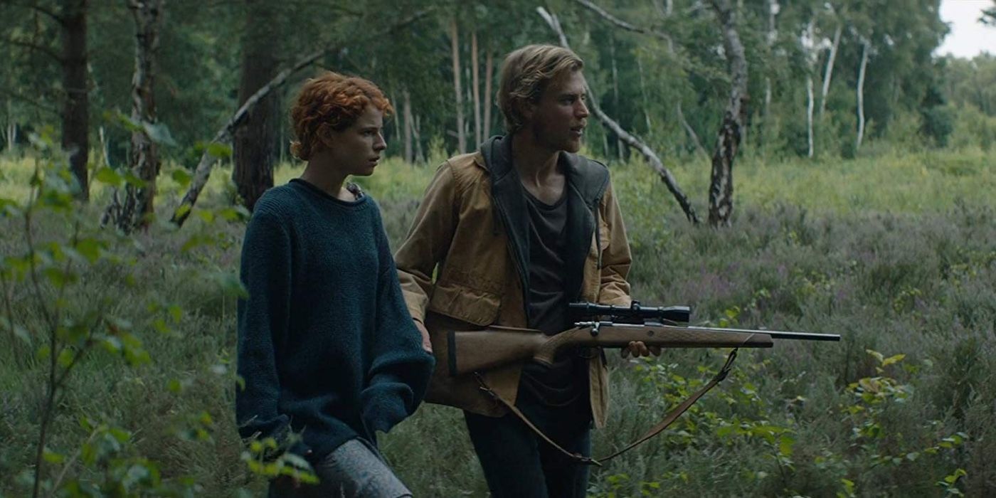 Jessie Buckley and Johnny Flynn with a gun walking in the woods in Beast