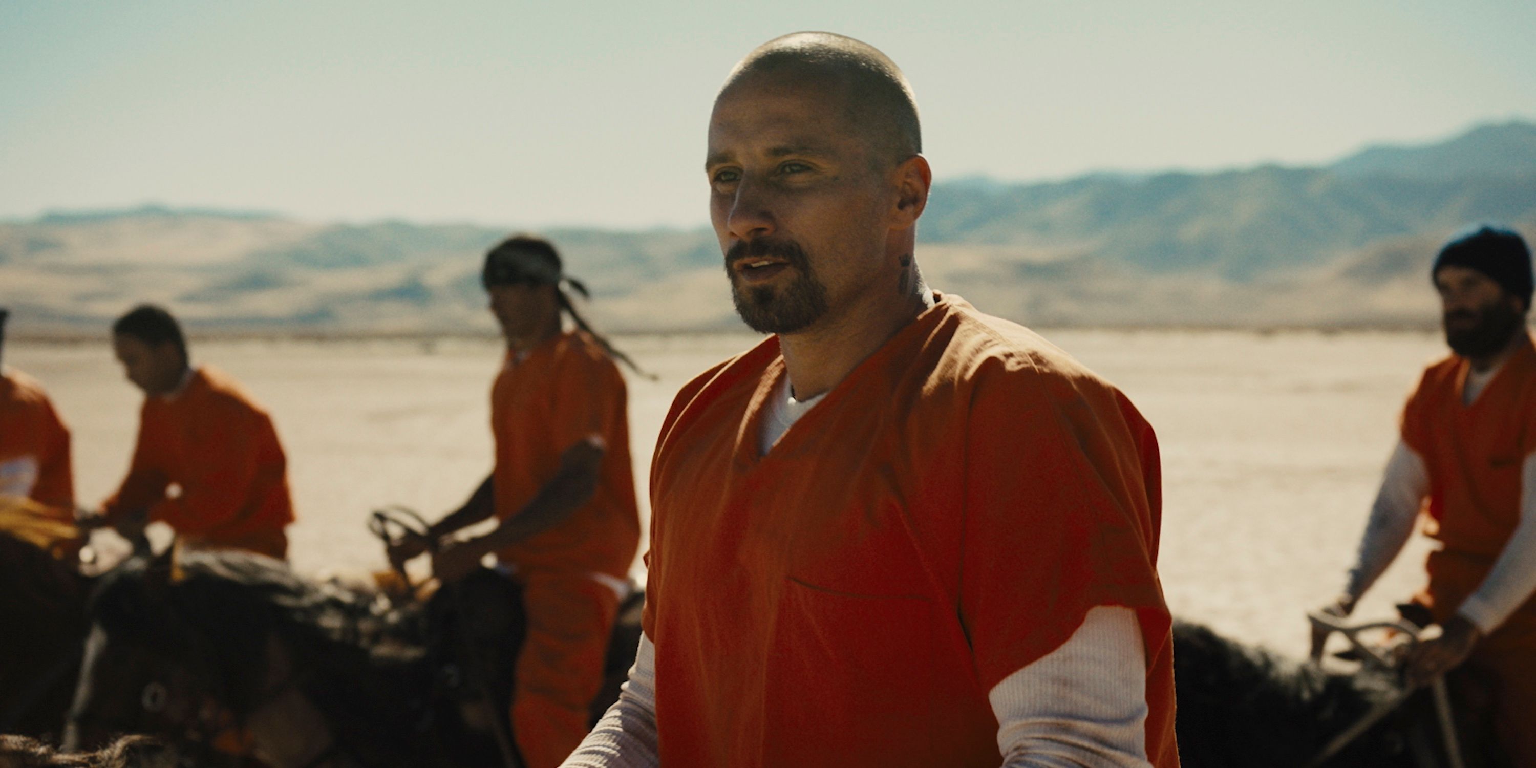 Matthias Schoenaerts and a group of men dressed in prison uniforms riding horses in The Mustang