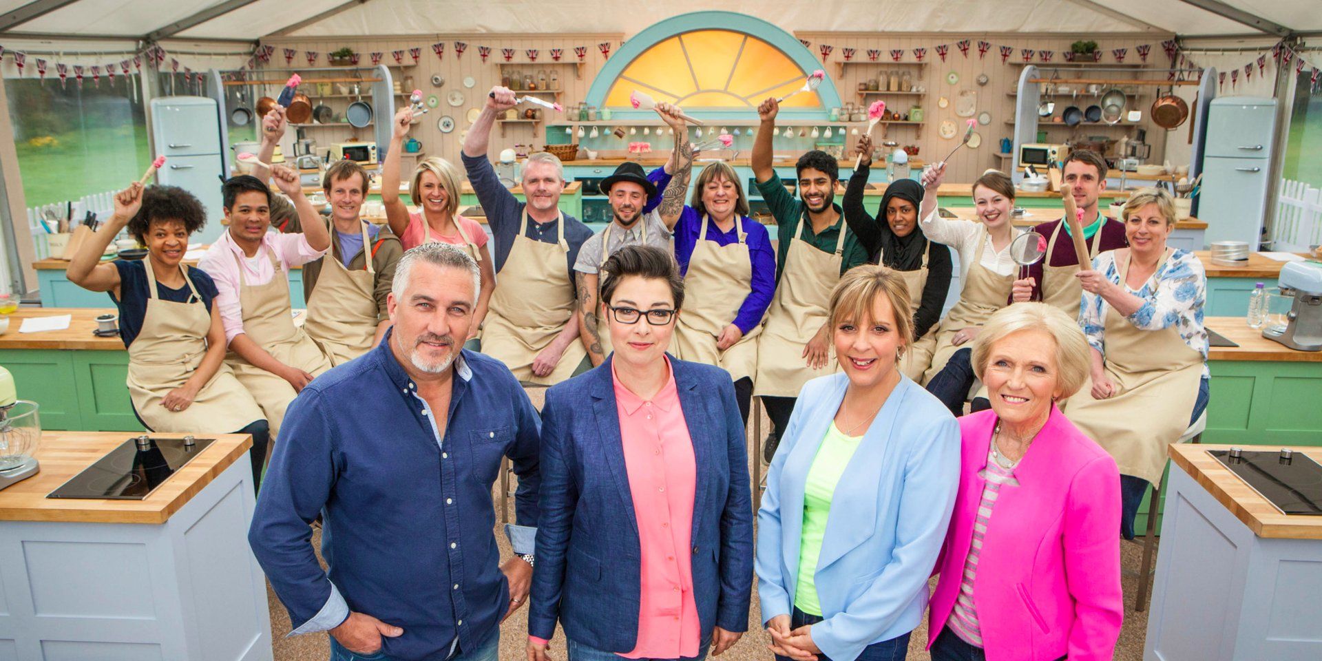 The Great British Bake Off's cat and contestants from one season all posing for the camera.