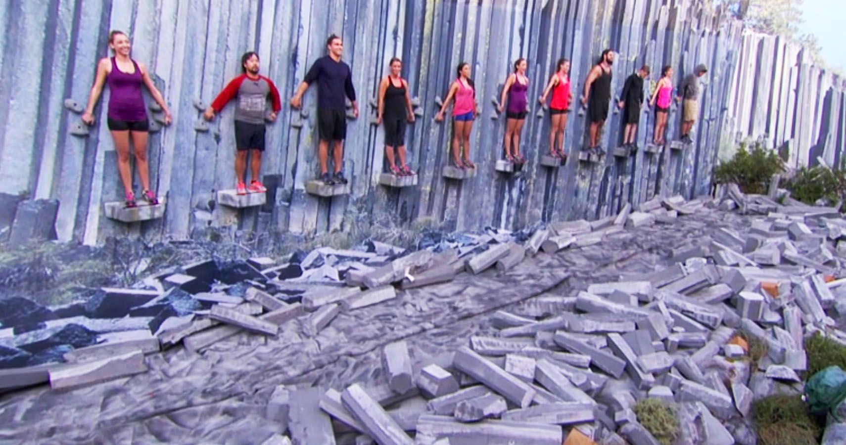 Players on Big Brother leaning against a wall, standing on a platform in an endurance competition.