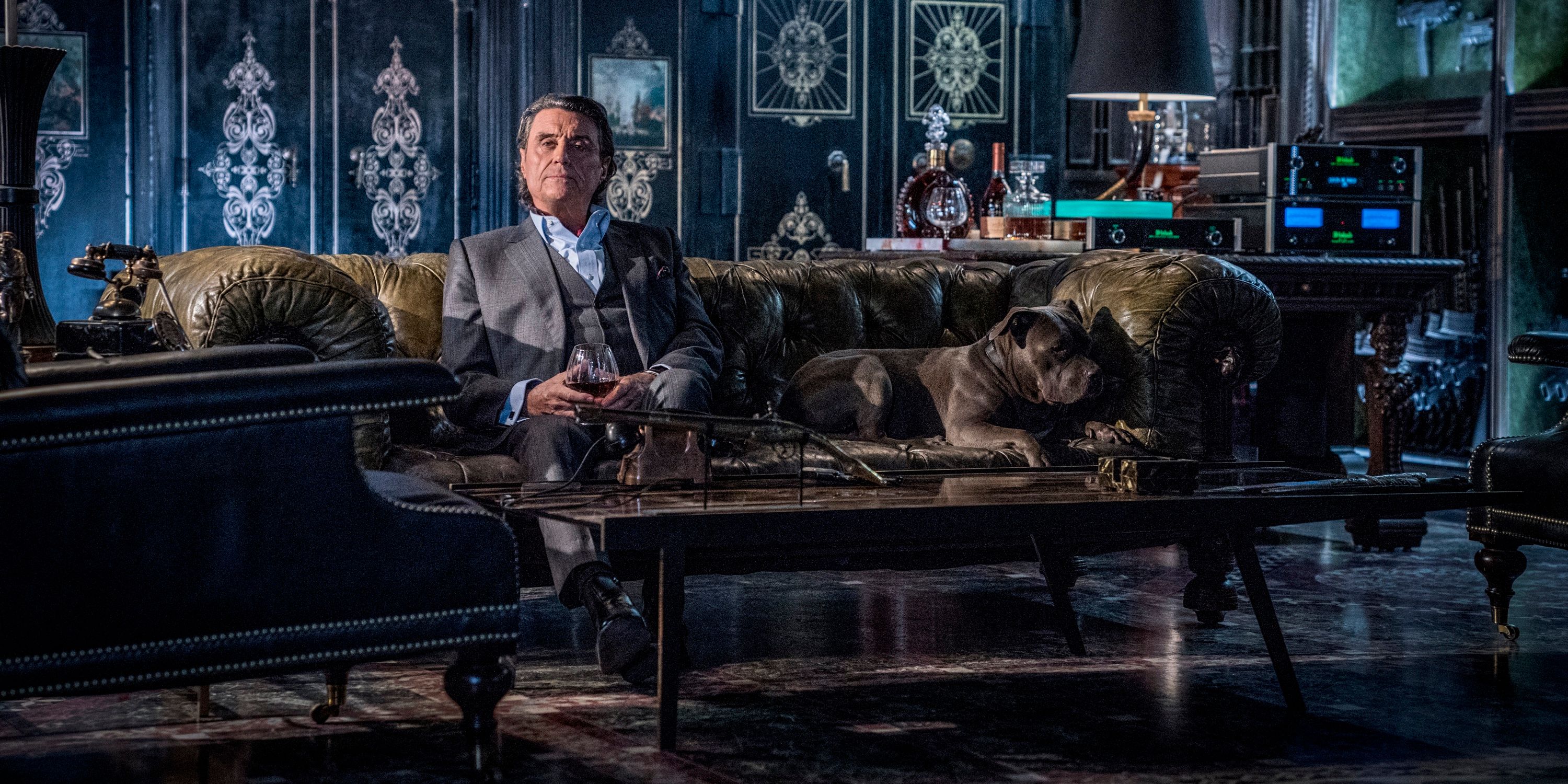 Ian McShan as Winston sitting on a sofa in John Wick 3