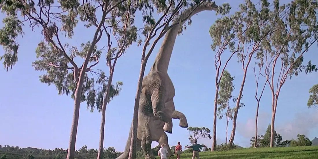 A brachiosaurus eats from the leaves as Ellie and Alan see a dinosaur for the first time in Jurassic Park