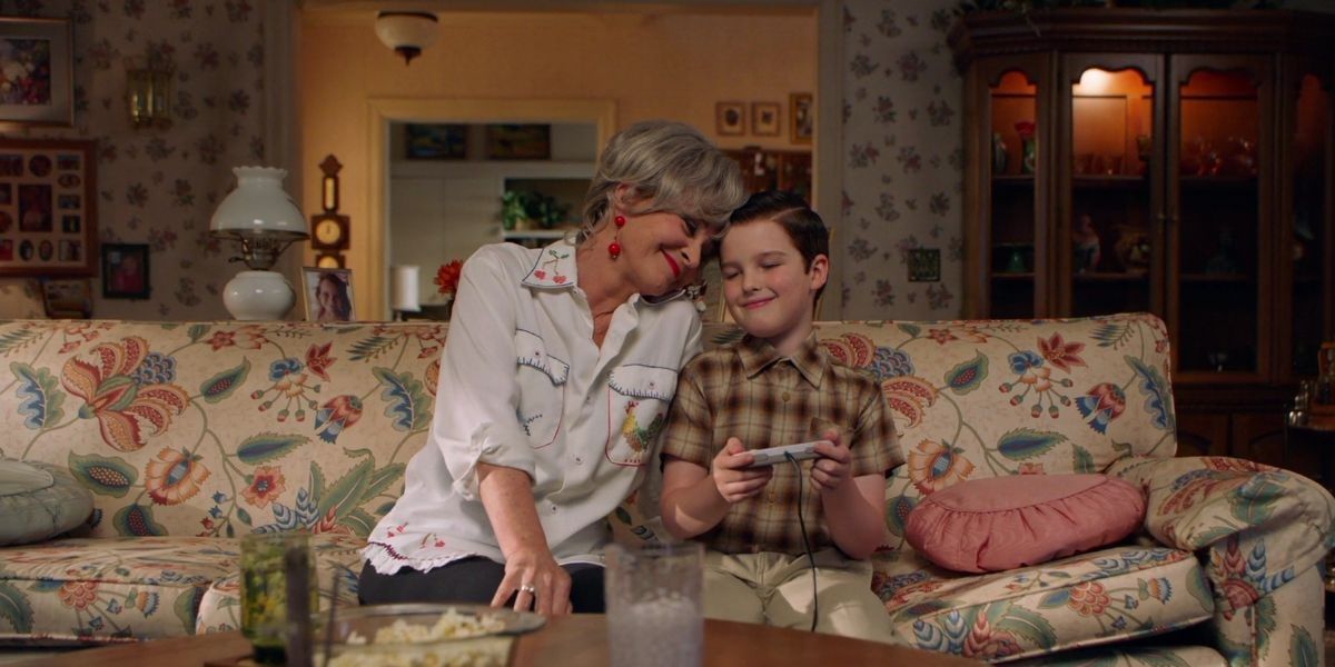 Sheldon and Meemaw from Young Sheldon on the couch smiling and playing video games together.